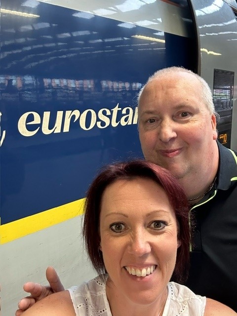 Andrew and Sara, the Group Lead Directors for Quality and Involvement at Thera Trust, take a selfie with the dark blue Eurostar train in the background on their travels to British Ambassador’s Garden Party in Paris. 